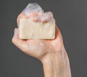 Close-up of a caucasian male hand holding a bar of soap aloft in his fist, isolated against a grey background.