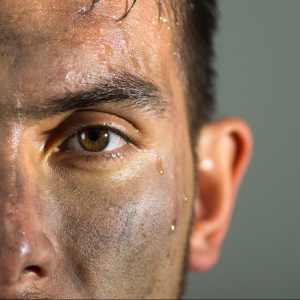 Closeup of a hispanic man with a dirty face looking to camera. His hair is untidy and a bead of perspiration runs down his cheek.