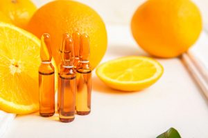 A shot of oranges on a white tablecloth, along with brown pharmaceutical ampoules filled with vitamin C serum.