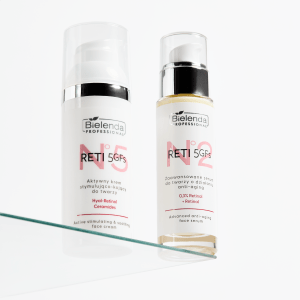 Product shot of two retinoid serums from BIELENDA PROFESSIONAL, one in an opaque white plastic bottle, the other in a see-through glass bottle with silver pump. The bottles are shown next to each other on a glass shelf against a white background.