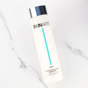 Product shot of the Creamy Cleansing Gel from SKINARTÉ, showing an elegant white bottle with a silver cap resting on a white and grey marble background.
